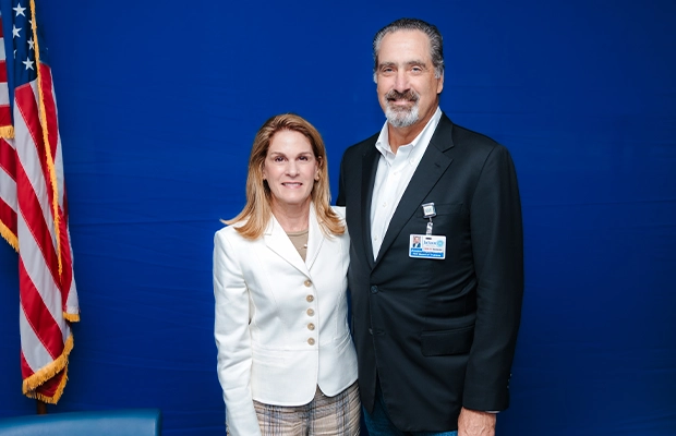 A man and a woman in formal wear smiling at the camera next to the United States flag.
