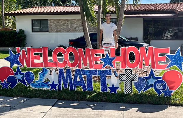 young man next to sign that says welcome home
