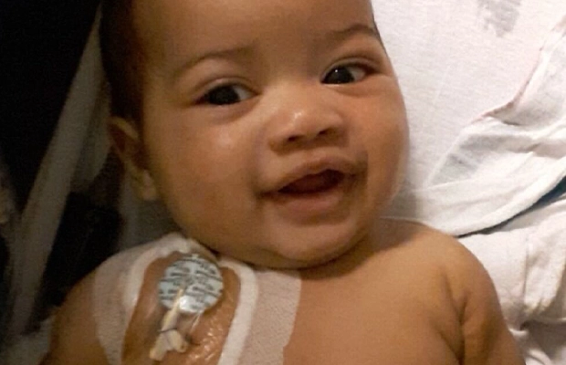 A baby smiling at the camera with a bandage on her shoulder