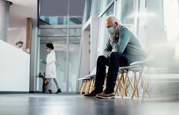 Adult man sitting in a hospital waiting room while wearing a face mask.