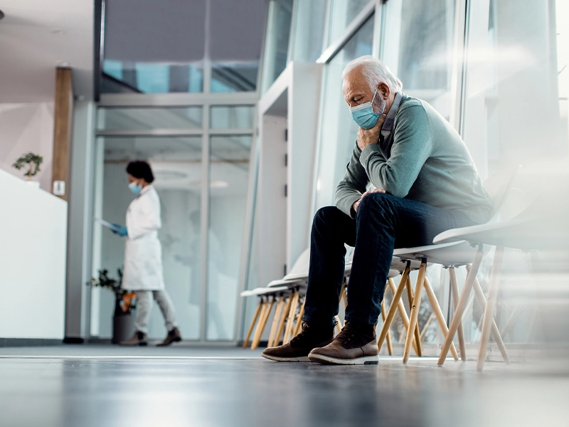 Adult man sitting in a hospital waiting room while wearing a face mask.