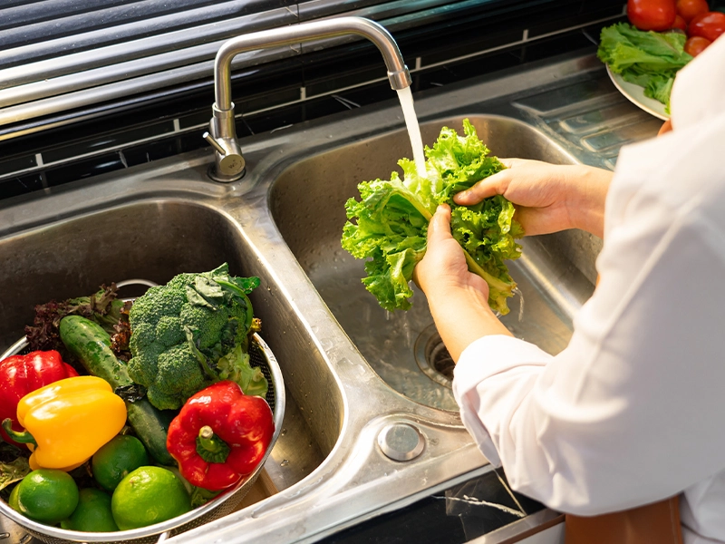 Close-up of a person's hands washing vegetables in the kitchen sink.