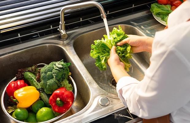 Close-up of a person's hands washing vegetables in the kitchen sink.
