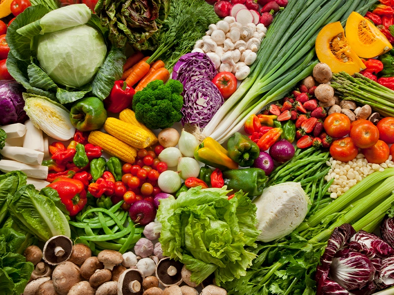 Photograph of a table full of vegetables such as onions, peppers, carrots, cucumbers, lettuce, mushrooms, and tomatoes, among others.