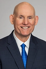 Headshot of David Ewing, he is looking at the camera, He is wearing a suit, with a white shirt and a blue tie.