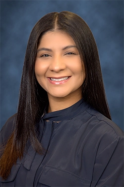 Close-up of a smiling woman dressed elegantly, with a blue background behind her.