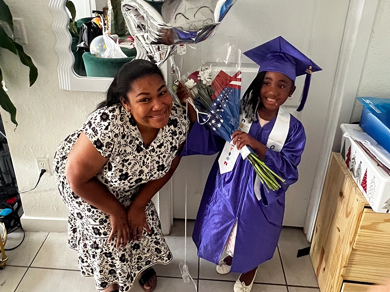 Photograph of a mother with her young daughter who is holding balloons.
