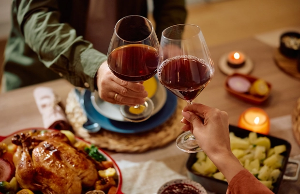 Close-up of two people toasting with glasses of red wine next to a table full of Christmas dishes