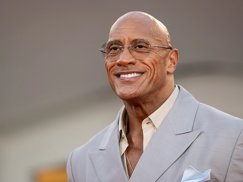 Close-up of The Rock, dressed in a wool suit, smiling during an event
