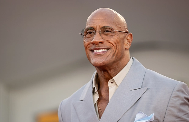 Close-up of The Rock, dressed in a wool suit, smiling during an event