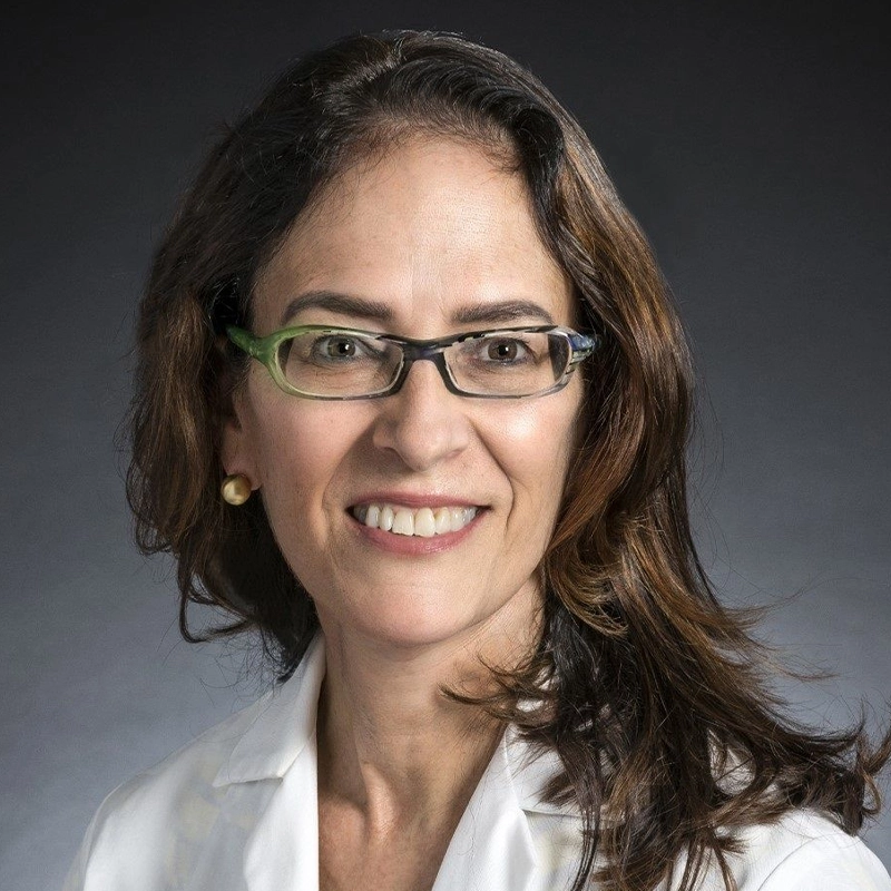 Close-up of a woman wearing a doctor's coat, with a dark gray background behind her.