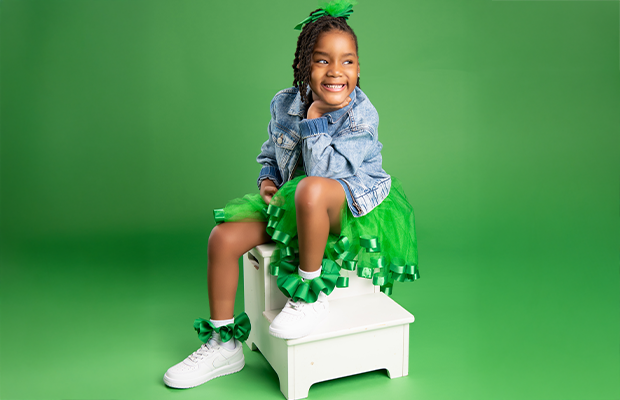 Little girl dressed in green sitting on a small white ladder, smiling and looking to the side.