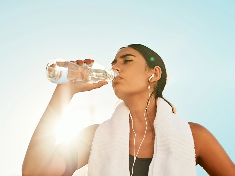 Medium shot of a woman drinking water outdoors, wearing sportswear.