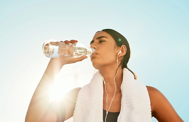Medium shot of a woman drinking water outdoors, wearing sportswear.