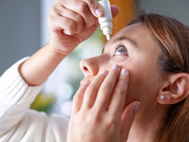 Close-up of a woman applying eye drops.