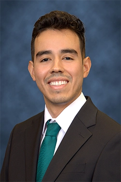 Close-up of a smiling man dressed elegantly, with a blue background behind her.