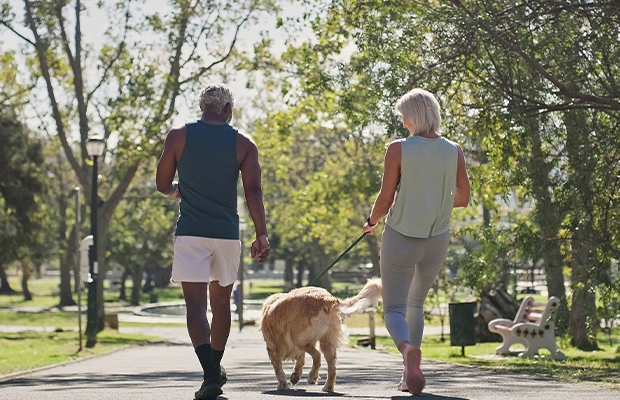 Two elderly adults walking in the park with their pet
