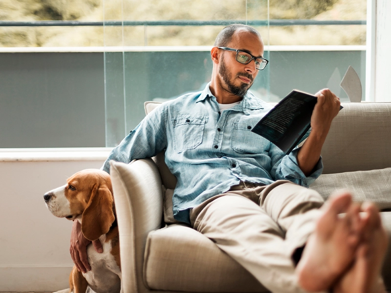 man sitting on the couch with his dog while reading