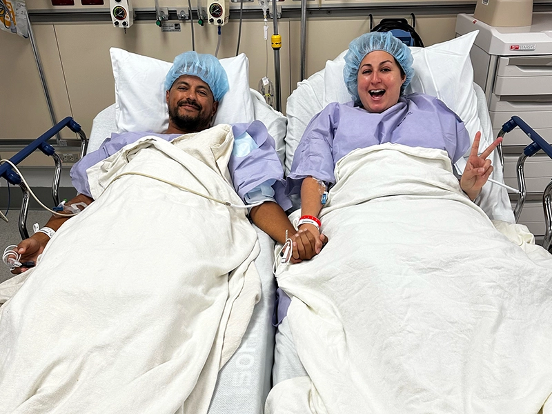 Man and woman lying on hospital stretcher while holding hands