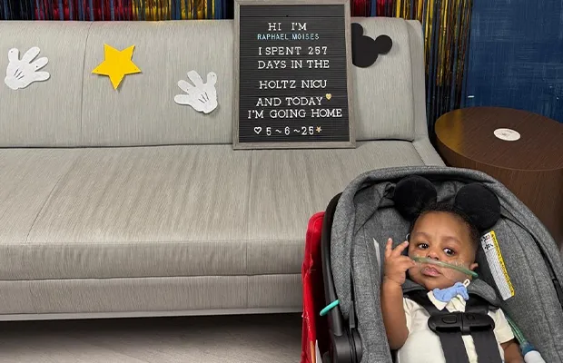 A baby in a car seat next to an advertisement containing text