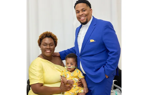 Woman dressed in yellow holding her baby next to a man in a blue suit