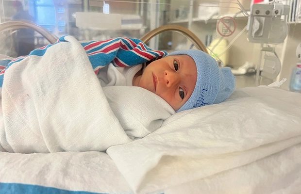 Baby lying in an incubator, looking at the camera.