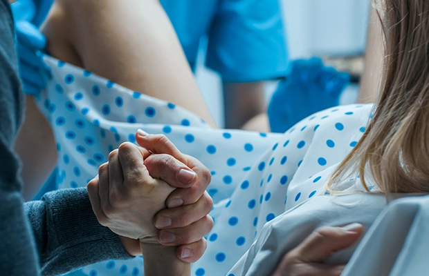 woman giving birth, while holding her partner's hand