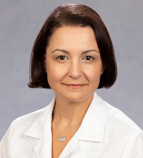 A woman smiling at the camera, she has short black hair, she has on a white coat