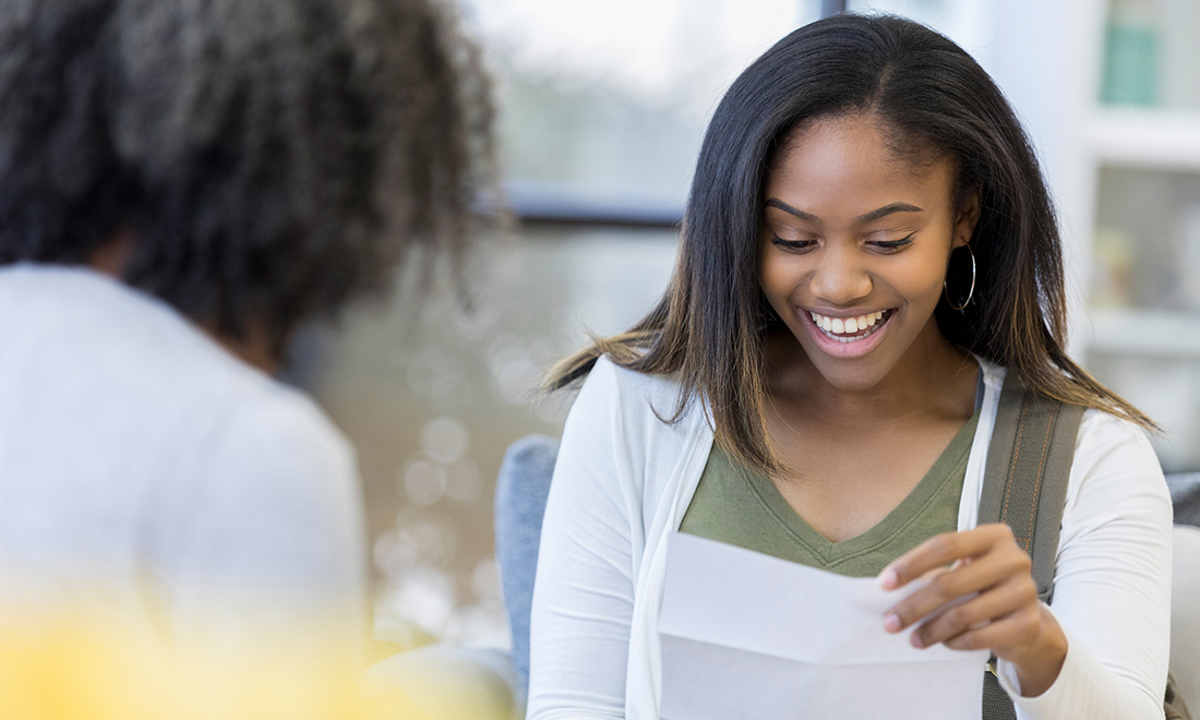 Excited woman reading an acceptance letter, she sits across another woman