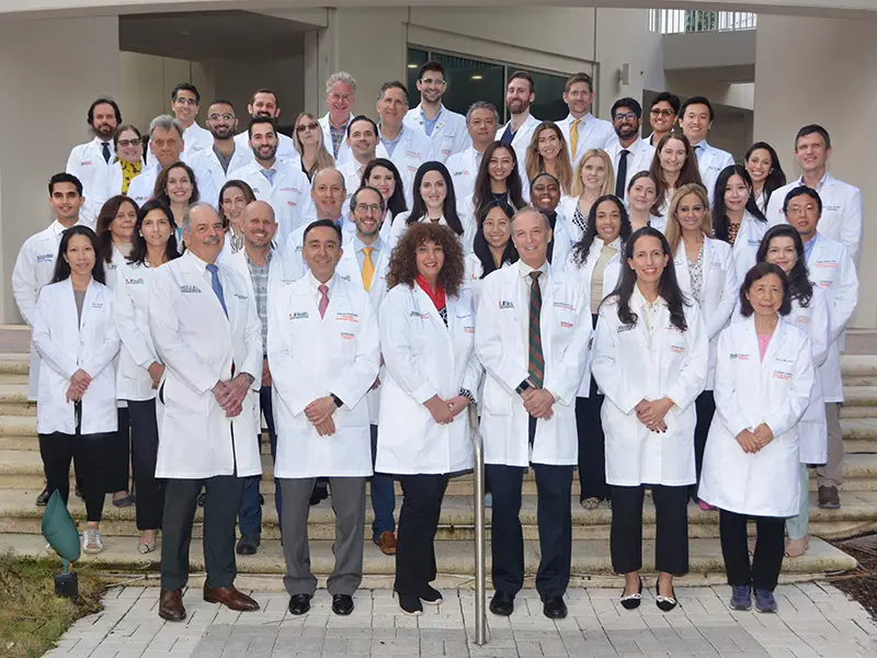A large group of medical professionals standing outdoors, they all look towards the camera