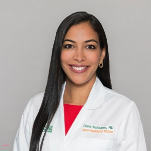 Headshot of Diana Molinares, she smiles at the camera, has long black hair, has on a black shirt and white coat