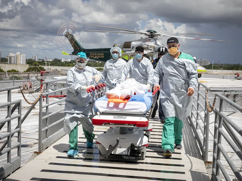 group of doctors carrying person on stretcher with helicopter behind them