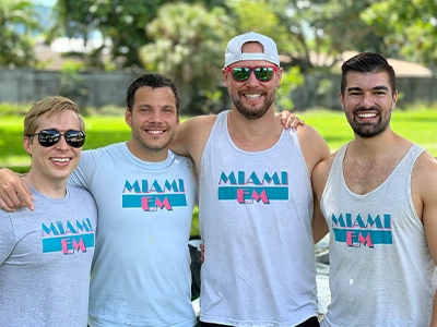 four men wearing the same t-shirt pose and hug the camera