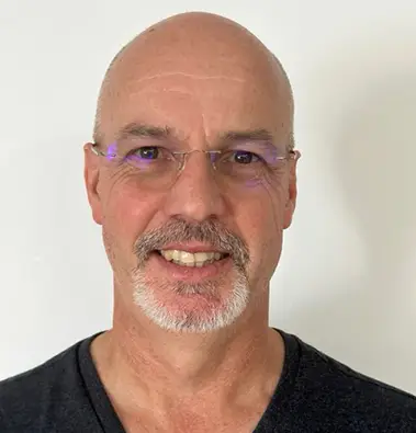 A closeup of a man, he has on glasses, and smiles at the camera