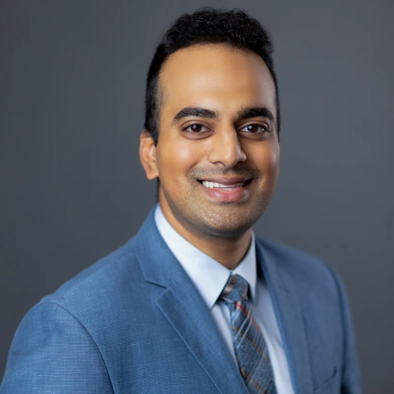 A headshot of a medical professional, he has on a blue coat