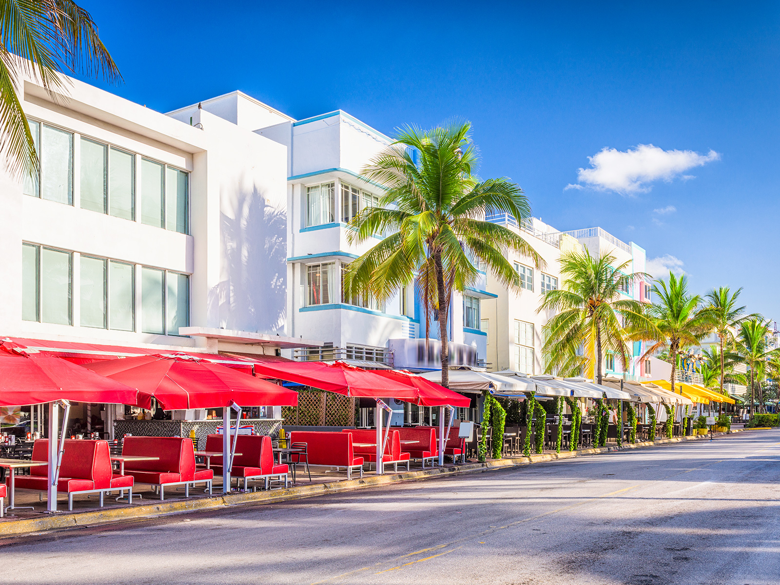 A view of multiple buildings in Miami Beach,the buildings are colorful, there is sitting and palm trees outside