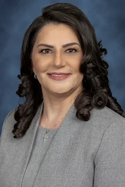 A headshot of a woman with curly dark hair, she smiles at the camera