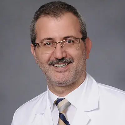 A medical professional smiling at the camera, he has on glasses, a white coat, and tie