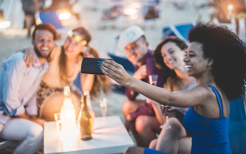 Friends smiling, they are outside near the water and one of the friends is taking a selfie