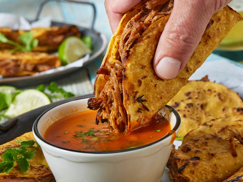 Close-up of a hand dipping a tortilla in birria