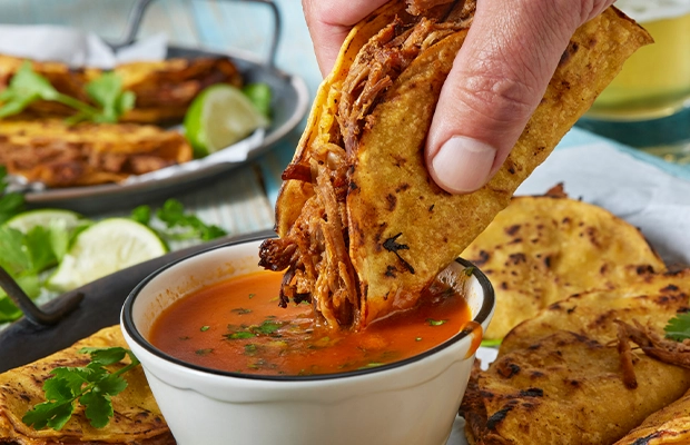 Close-up of a hand dipping a tortilla in birria