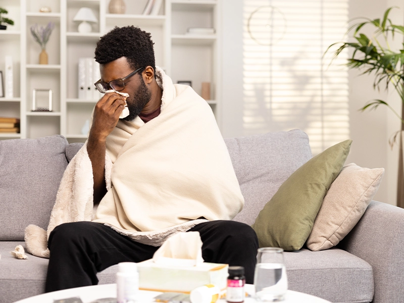 Sick man sneezing while sitting on a sofa using a blanket
