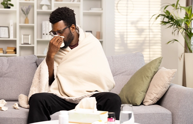 Sick man sneezing while sitting on a sofa using a blanket