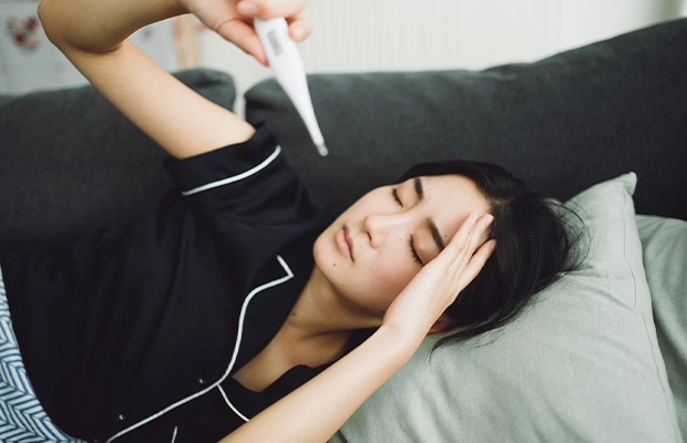 A woman lying down, checking a thermometer.