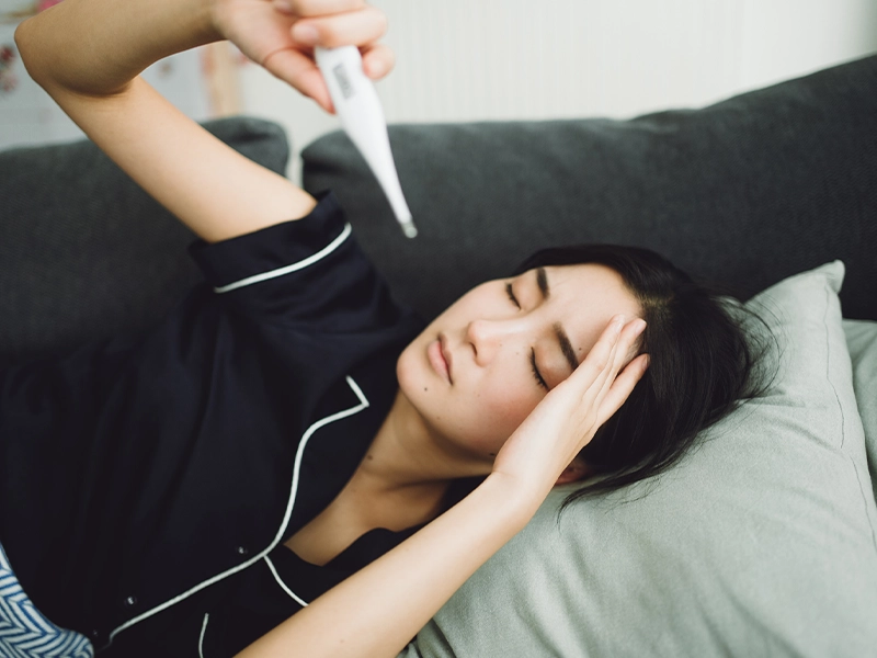A woman lying down, checking a thermometer.