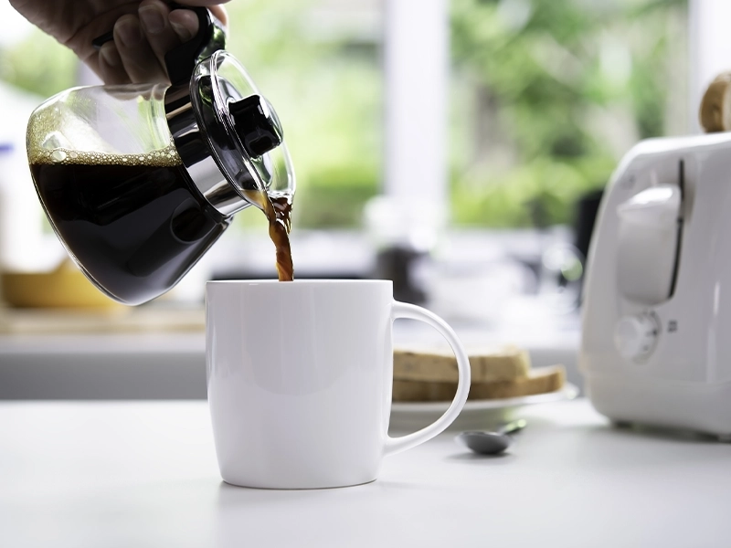 Close-up of a hand pouring coffee into a white cup