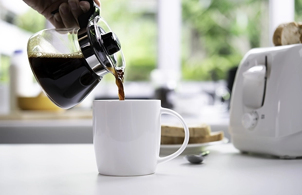 Close-up of a hand pouring coffee into a white cup