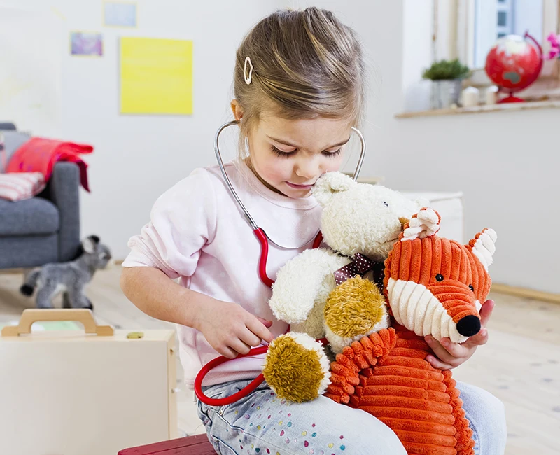A young girl playing with a stethoscope and her stuffed toys