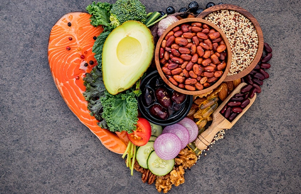 An image of food arranged in the shape of a heart; visible items include salmon, avocado, grains, onion, cucumber, and broccoli, among others.