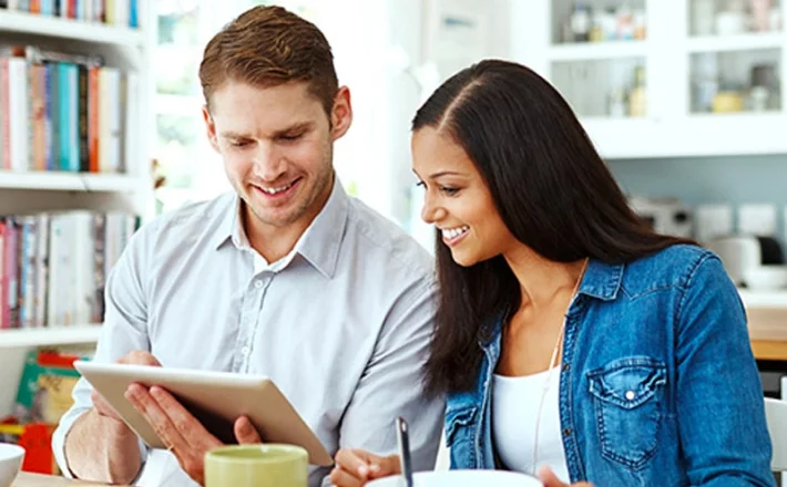 A man and women sitting and smiling, they look at a tablet